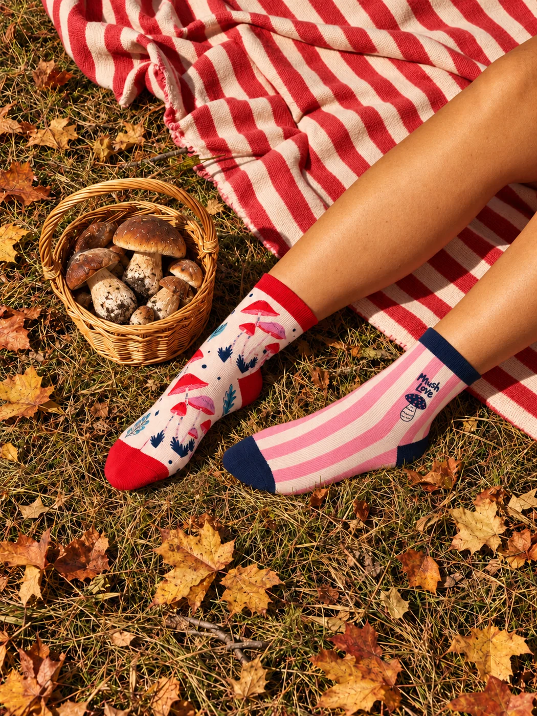 Deux modèles Woodland portés lors d’un pique-nique automnal : chaussettes crème à champignons et modèle à rayures roses, près d’un plaid rouge et d’un panier de champignons